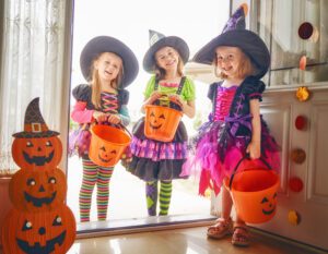 Three young girls in witch costumes with pumpkin buckets going trick or treating for Halloween