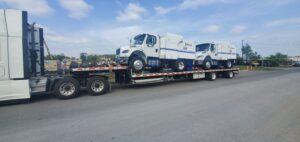 A flatbed truck containing two brand new XBroom heavy duty sweepers